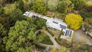 An aerial view of a modern house with solar panels, surrounded by dense greenery and trees. - StayAU 4BR Spacious Nature Retreat (Badger Creek)