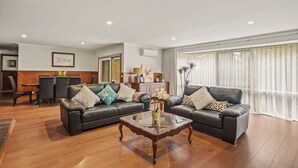 A modern living room with two leather sofas, a glass coffee table, and a dining area with a wooden table and chairs. - StayAU 4BR Spacious Nature Retreat (Badger Creek)