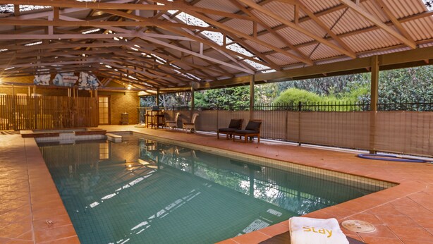 An indoor swimming pool with a tiled floor, a bench with a towel, and a covered area with chairs and a fence. - StayAU 4BR Spacious Nature Retreat (Badger Creek)