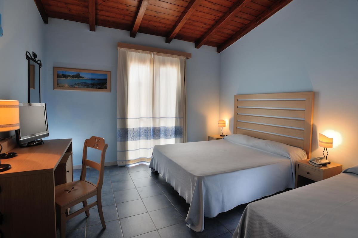Een slaapkamer met twee bedden, een bureau met een computer, een stoel en een raam met gordijnen.