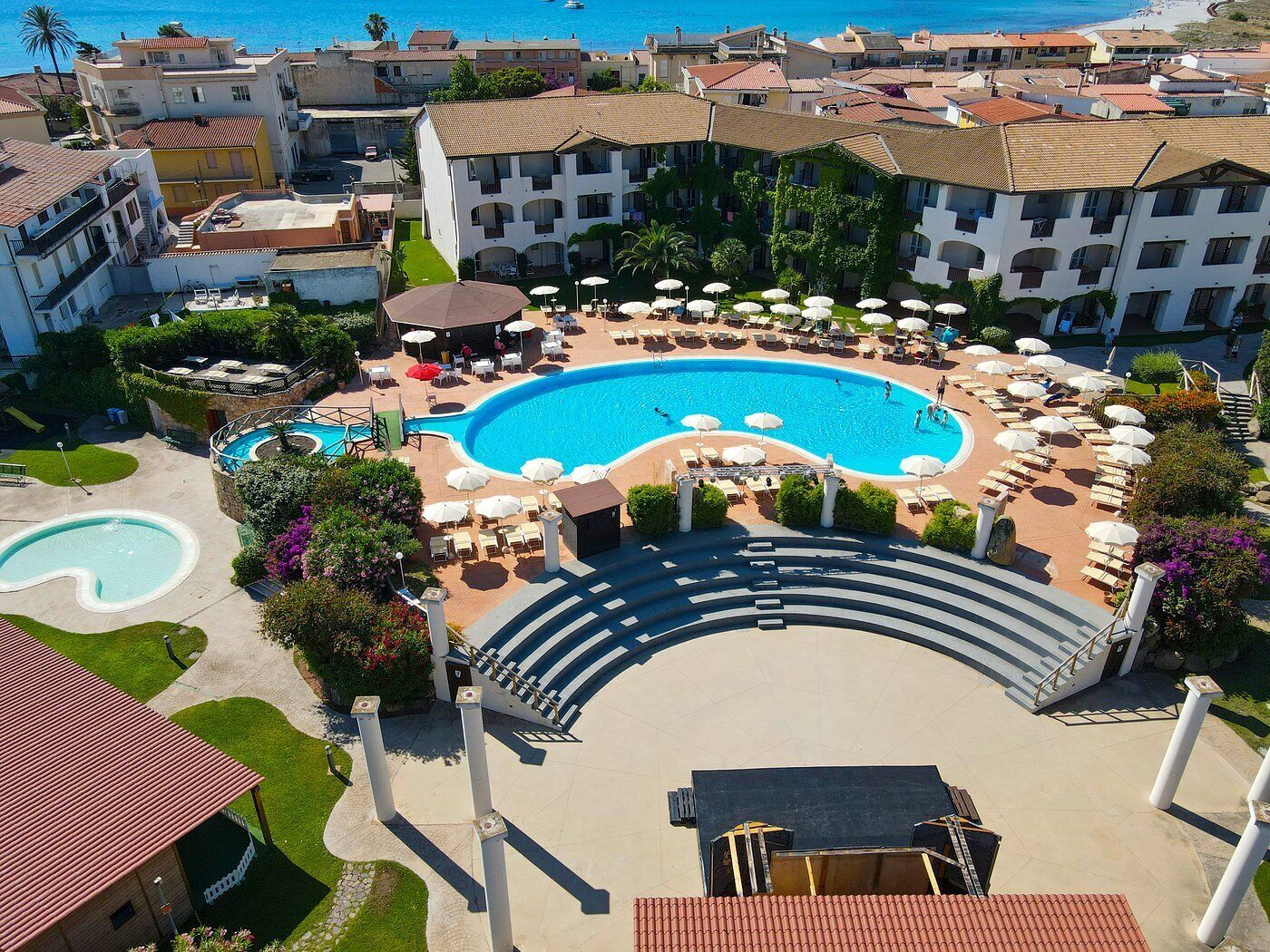 Um resort com uma grande piscina central, espreguiçadeiras e uma escadaria que dá acesso à área da piscina.