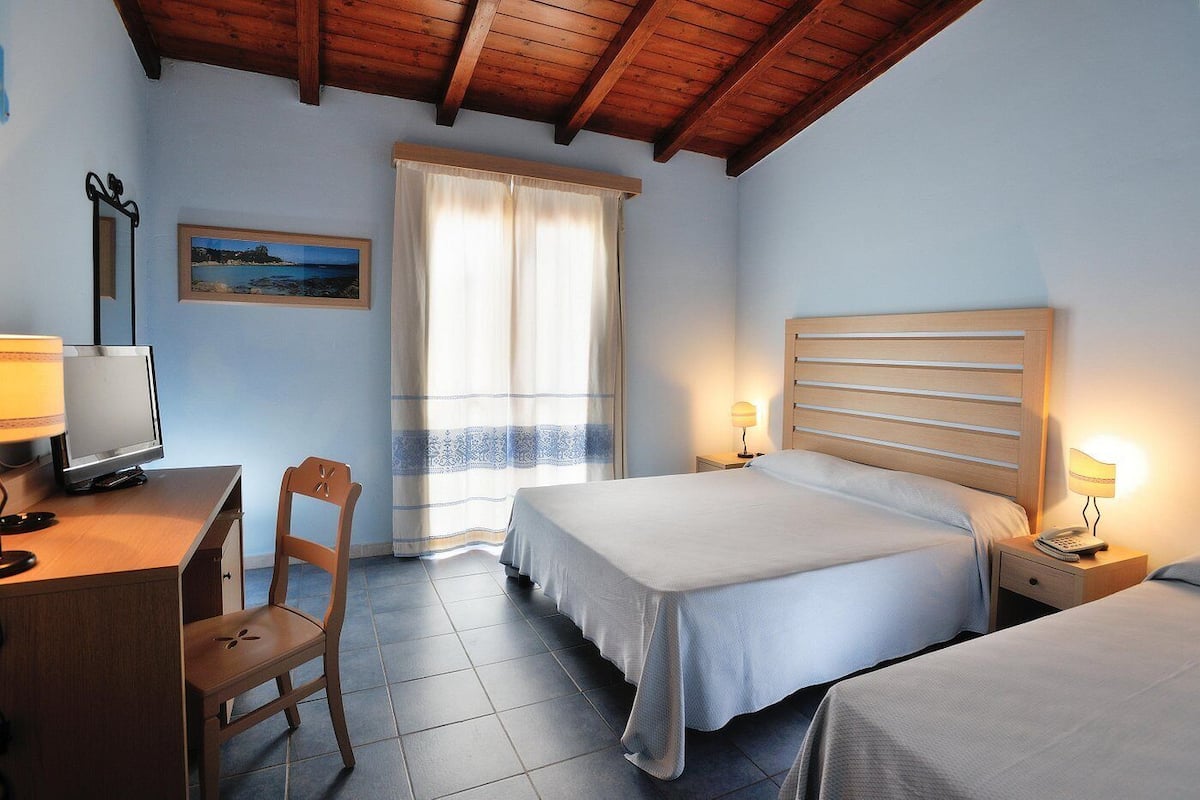 Een hotelkamer met een bed, nachtkastjes, een bureau met een computer, een stoel en een raam met gordijnen.