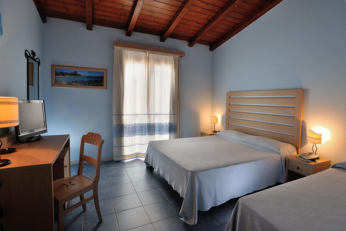 Un dormitorio con dos camas, un escritorio con computadora, una silla y un ventanal con cortinas.
