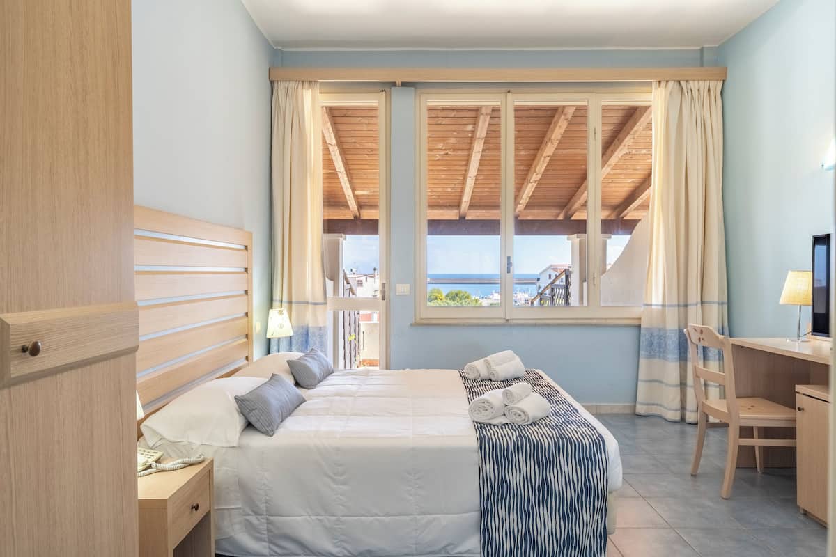 Een slaapkamer met een bed, een bureau en uitzicht op zee.