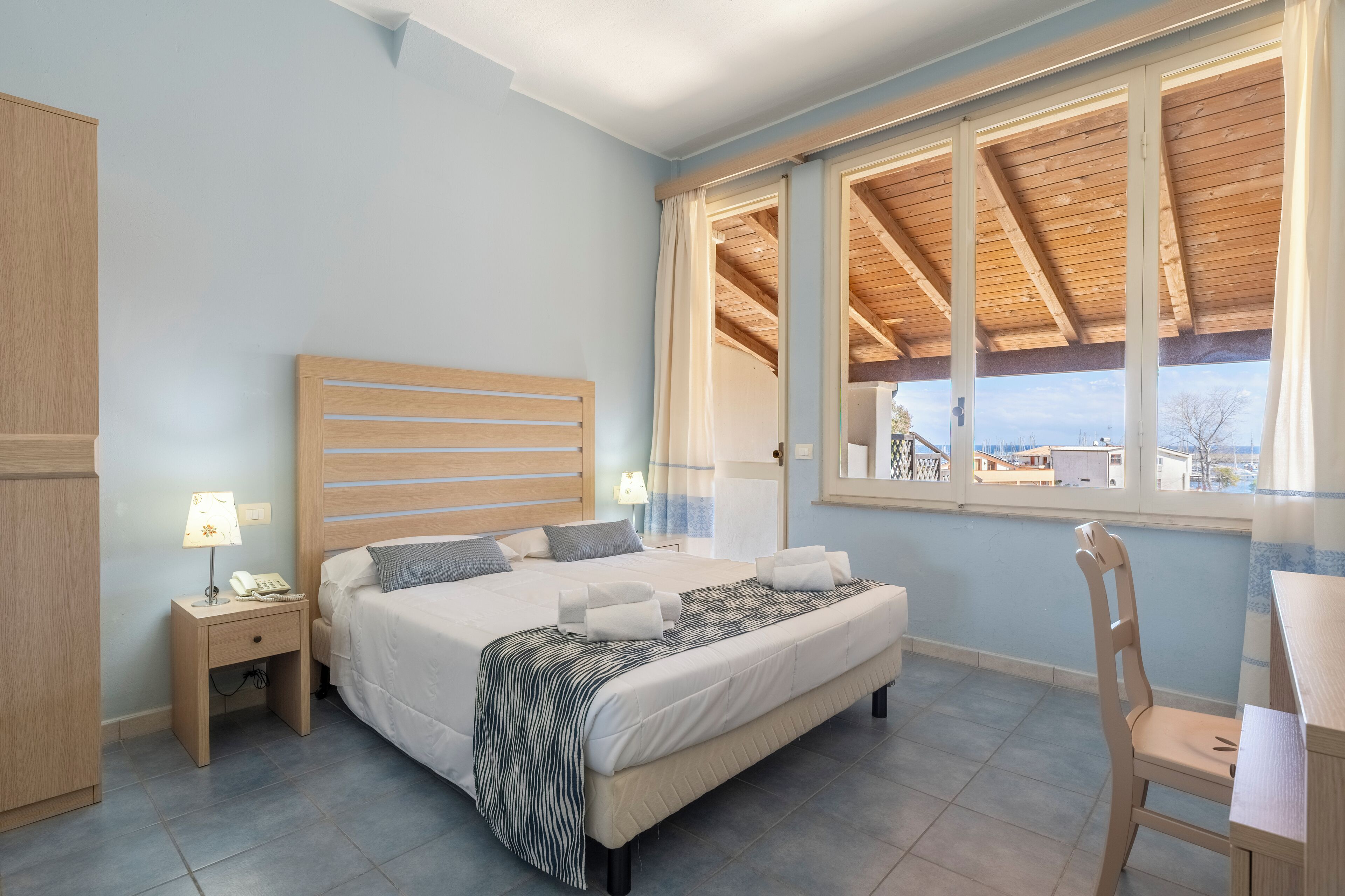 Ein Schlafzimmer mit Bett, Nachttisch, Lampe und Blick durch ein Fenster.