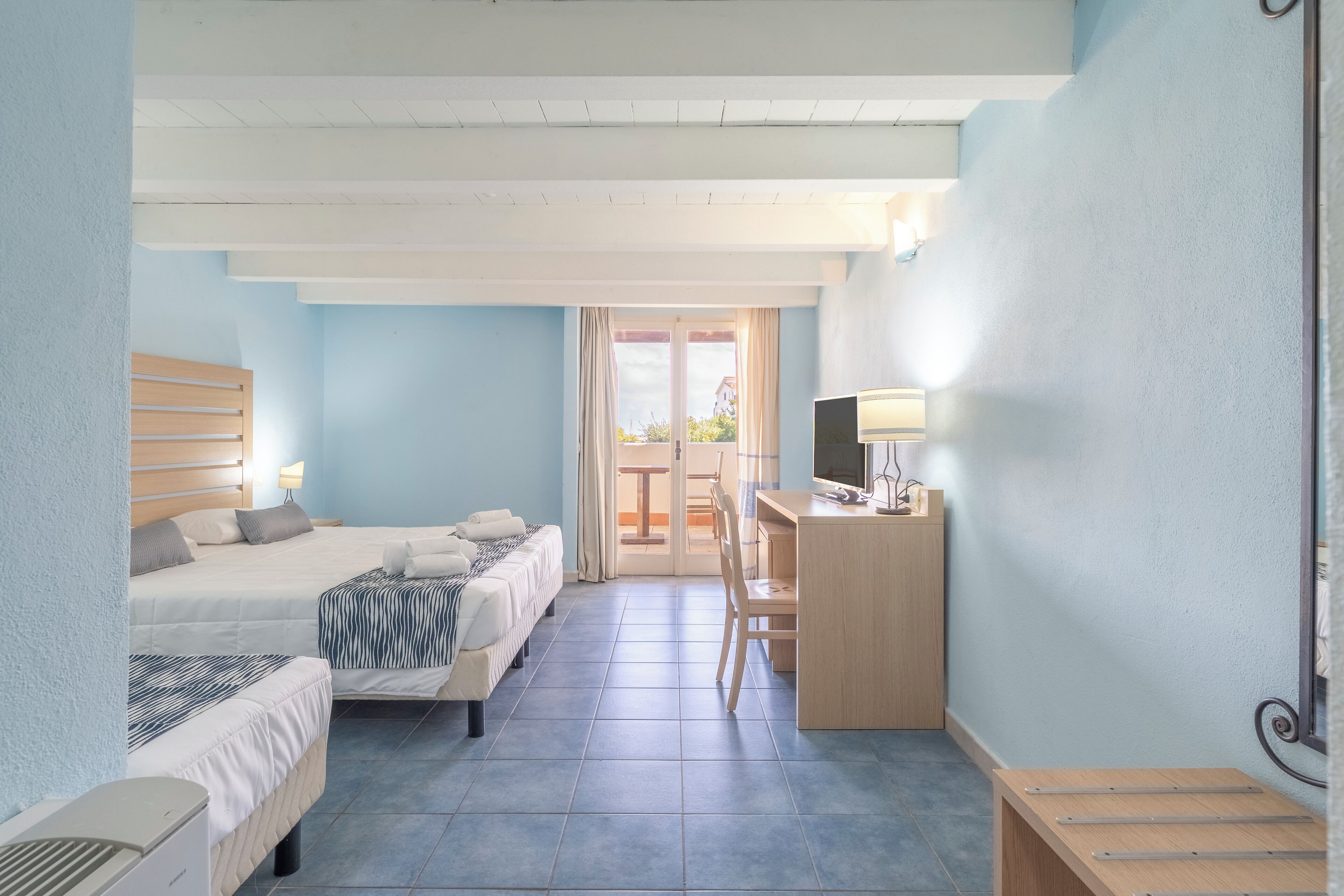 A hotel room with two beds, a desk with a computer, a chair, and a small table.