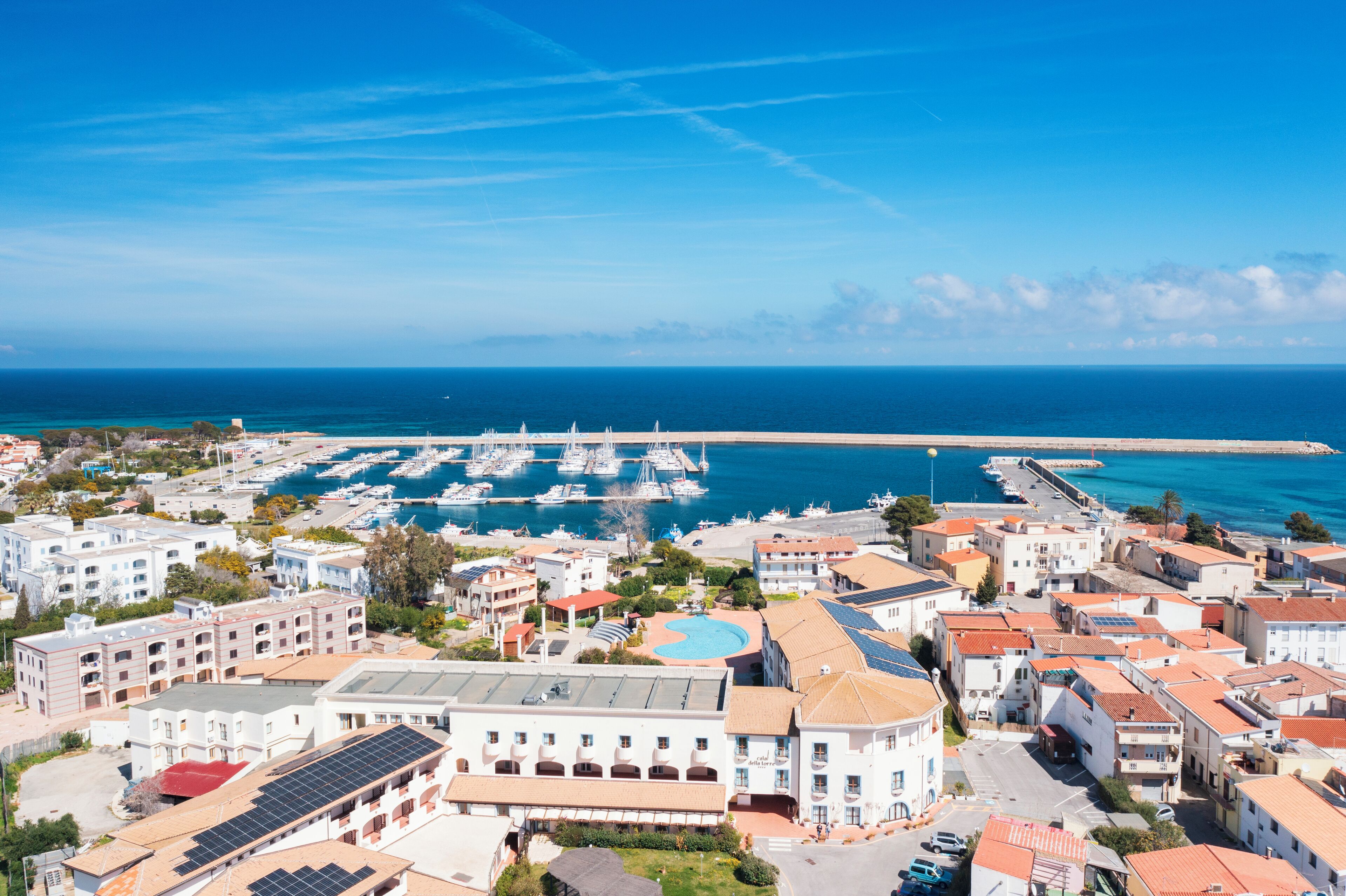 A coastal town with a marina, buildings with red-tiled roofs, and a clear blue sky.