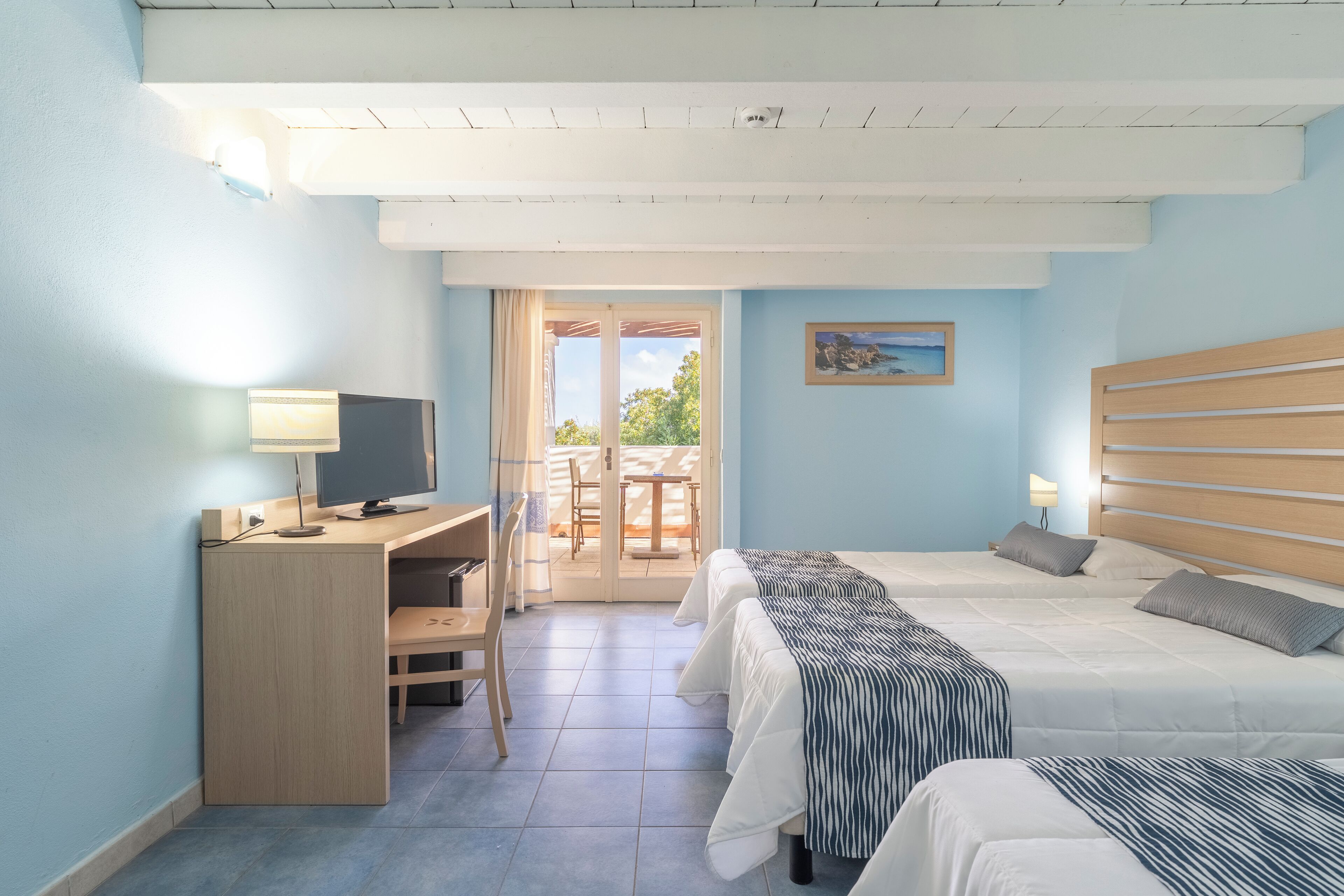 Quarto de hotel com uma mesa, duas camas, uma televisão e vista para o exterior.