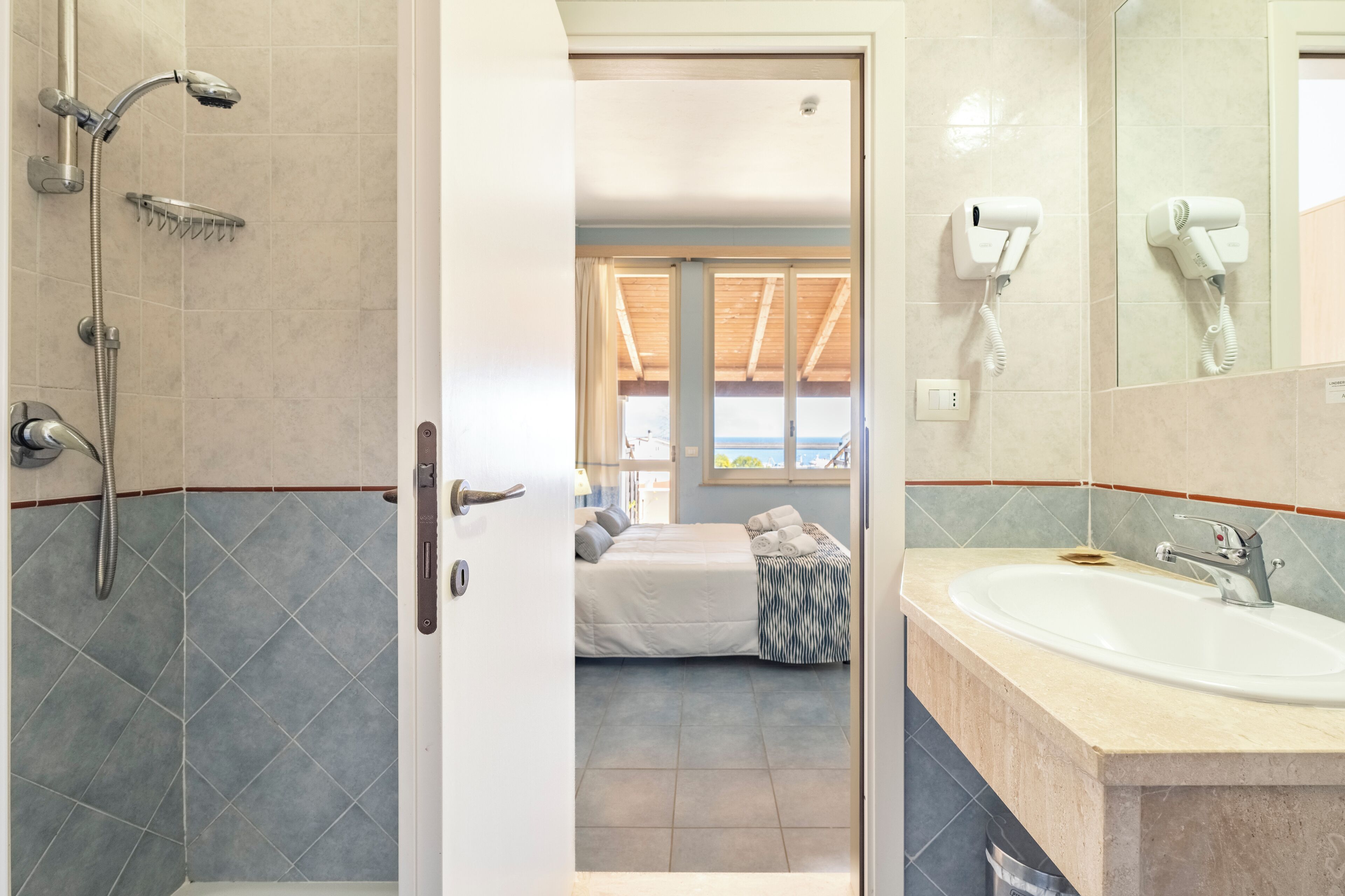 A bathroom with a shower, a sink, and a hairdryer mounted on the wall.