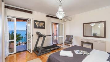 Un dormitorio con cama, cinta de correr, una silla, escritorio, espejo y vista al mar.
