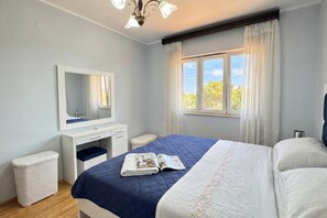 Un dormitorio con cama, mesita de noche, espejo, ventana con cortinas y luz en el techo.
