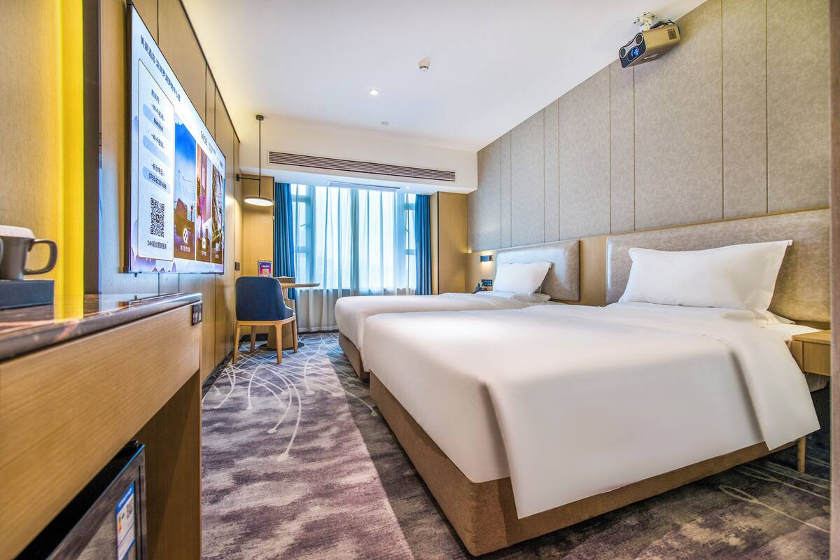 A hotel room with a large bed, a desk with a chair, and a window with curtains.