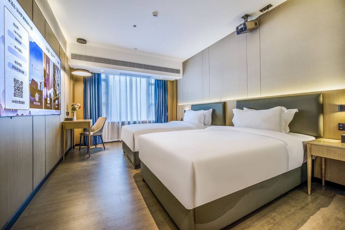 A hotel room with two beds, a desk, and a chair.