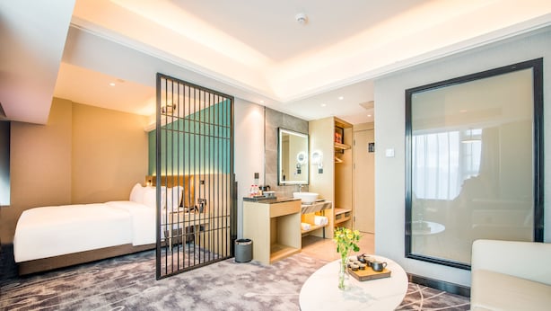 A hotel room with a bed, a small table with a vase, a bathroom with a sink and mirror, and a large window. - Meihao Hotel Shenzhen Sungang Branch (Shenzhen)