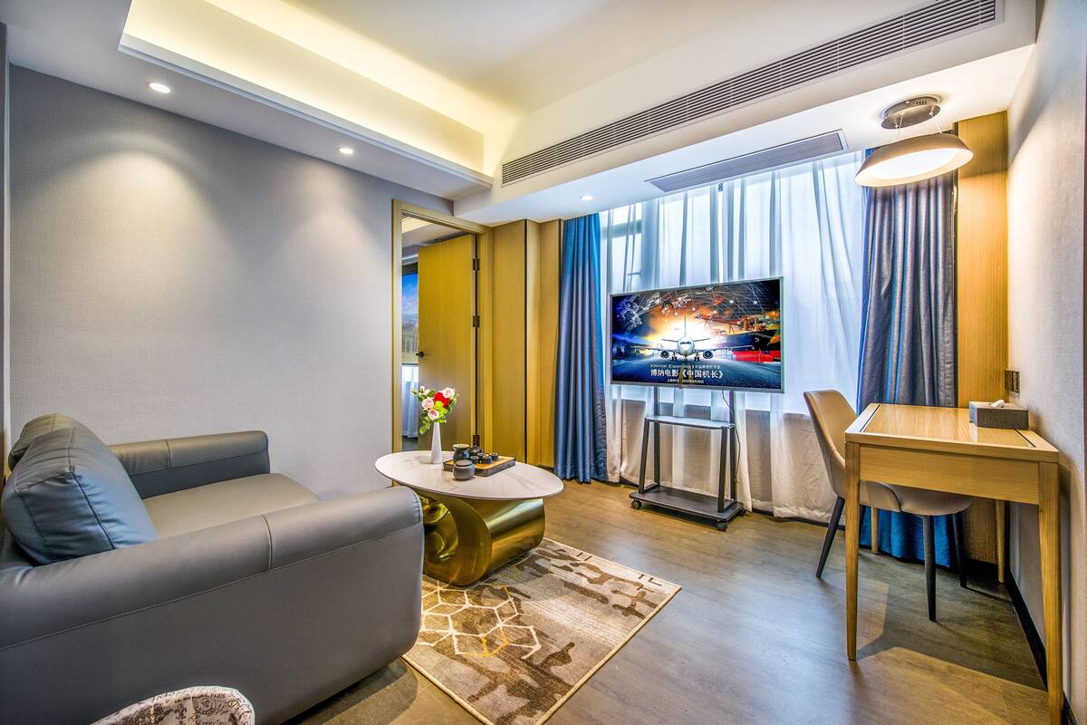 A modern living room with a sofa, coffee table, TV, and a dining area.