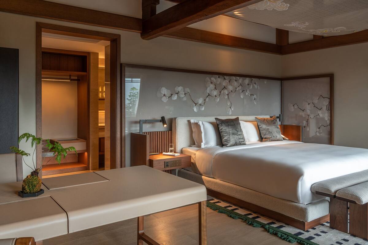 A modern bedroom with a large bed, bedside tables, a bench, and a built-in wardrobe.