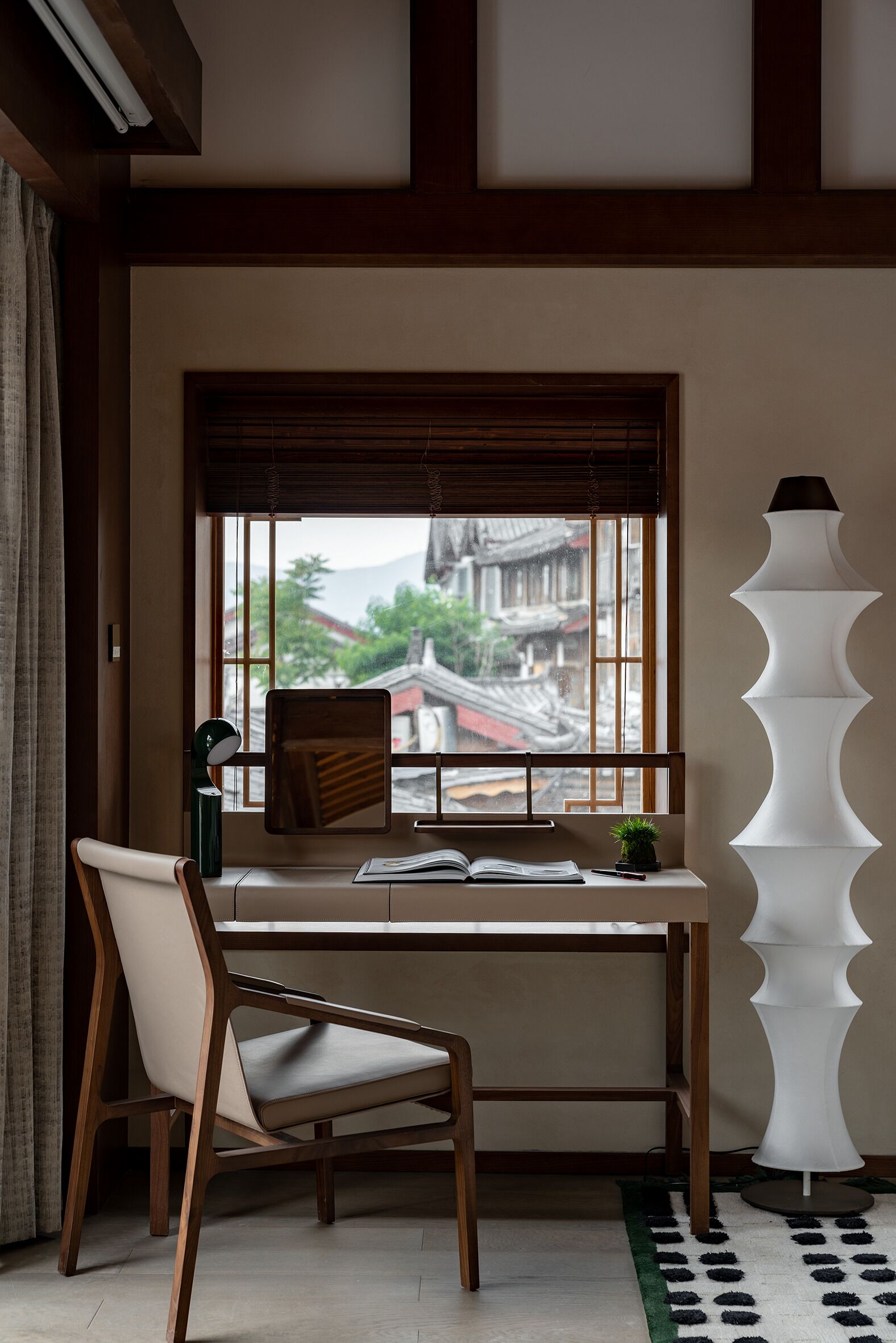 Ein Zimmer mit Schreibtisch, Stuhl, Lampe und Fenster mit Jalousien.
