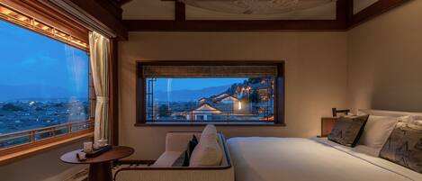 Habitación de hotel con una cama grande, una mesita con una silla, una ventana con vistas a la ciudad y un techo decorativo.