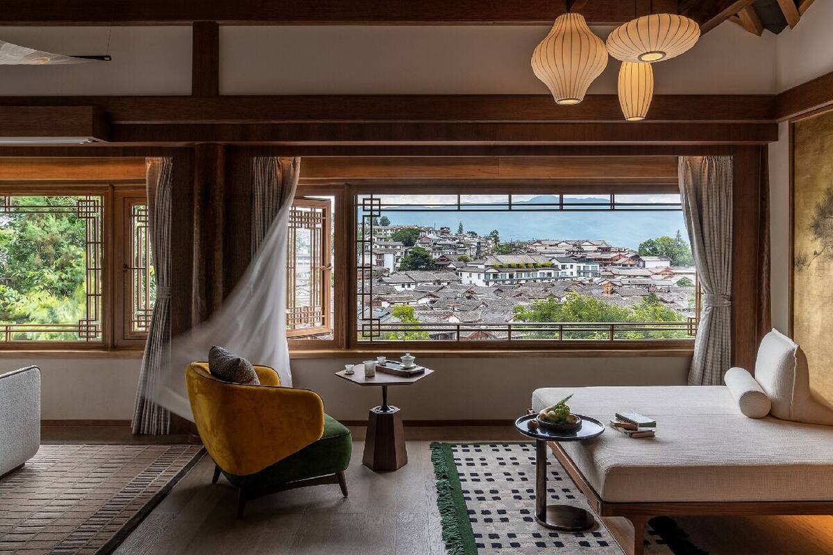 A room with a view of a cityscape through large windows, a yellow armchair, a white sofa, and a small table with a tray.
