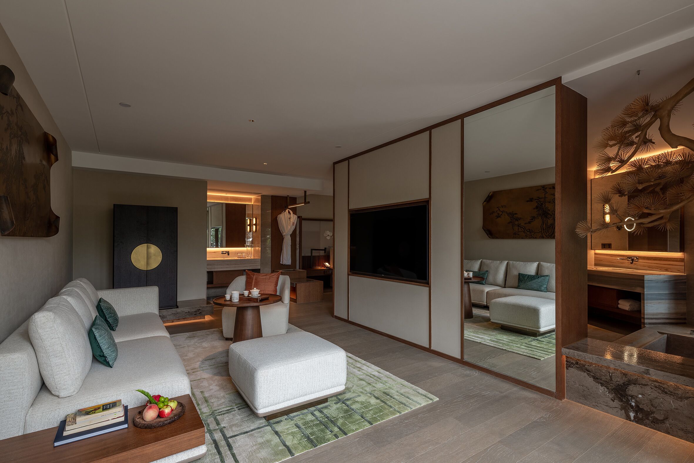 Een moderne woonkamer met een bank, een poef, en een salontafel, een grote flatscreen-televisie, en een decoratieve spiegel.