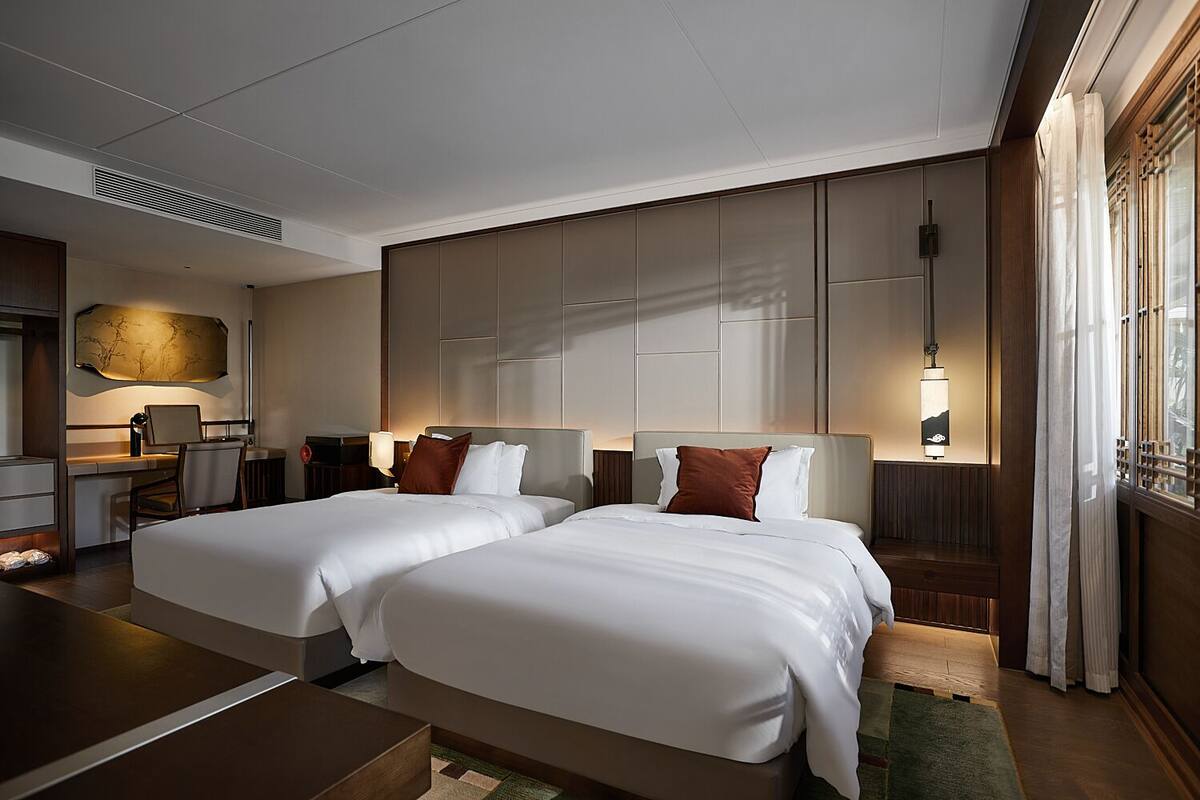 A hotel room with two beds, a desk, and a large wall-mounted artwork.