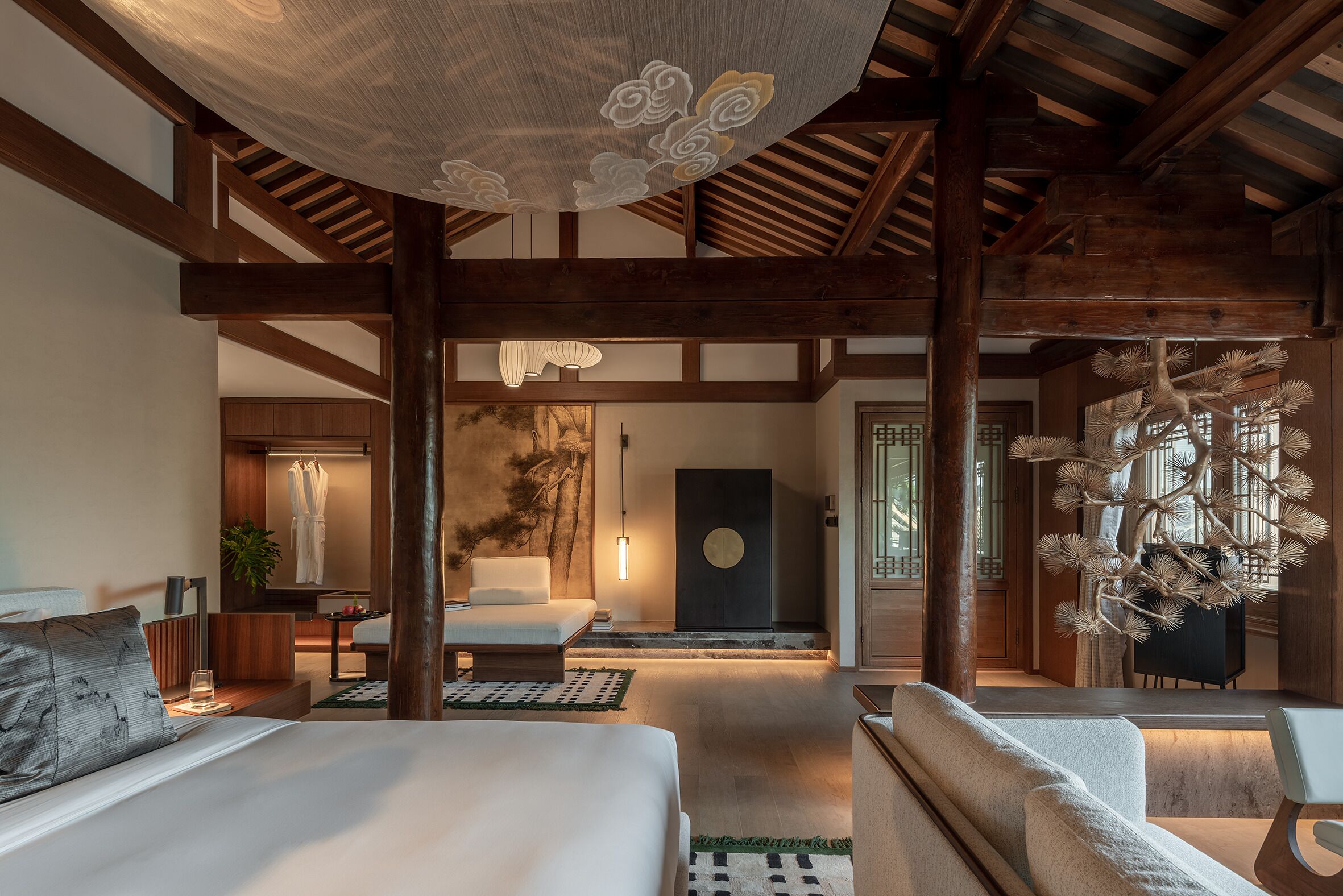 Una habitación de hotel moderna con una cama grande, un sofá, una zona de comedor y un techo de estilo tradicional con vigas de madera.