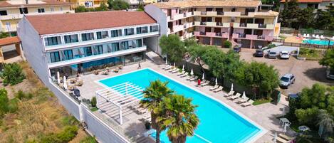 A hotel with a swimming pool, multiple balconies, and a view of the surrounding residential area.