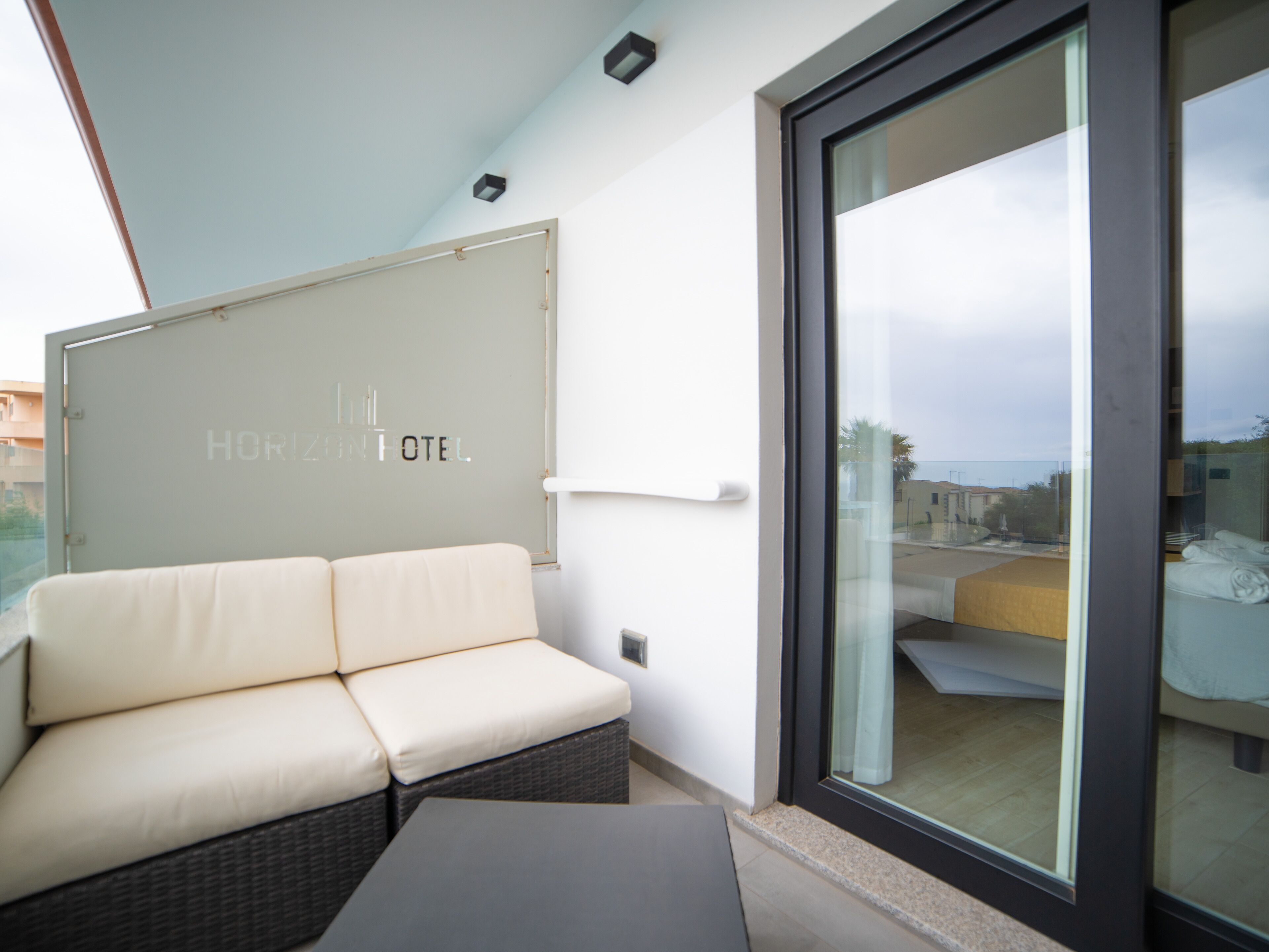 A modern hotel room with a sofa, a small table, and a large window offering a view of the city.