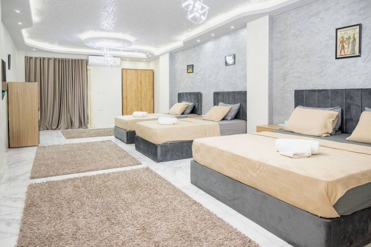 A hotel room with three beds, a wooden wardrobe, and a large window with curtains.