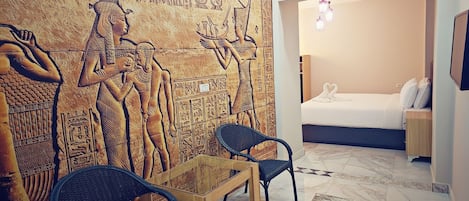 A room with a mural of ancient Egyptian hieroglyphs, a bed with white linens, and a small table with chairs.