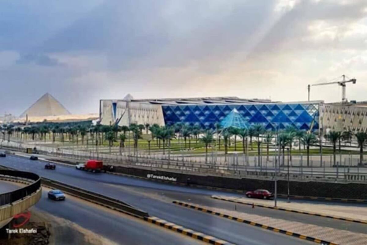 A modern building with a geometric facade, a highway with multiple lanes, and a pyramid in the background.