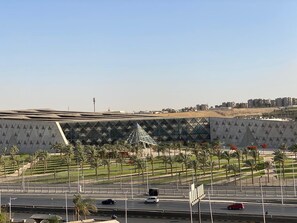 A large, modern building with a geometric facade, surrounded by a landscaped area with palm trees and a parking lot with cars. - GEM VIEW INN (Giza)