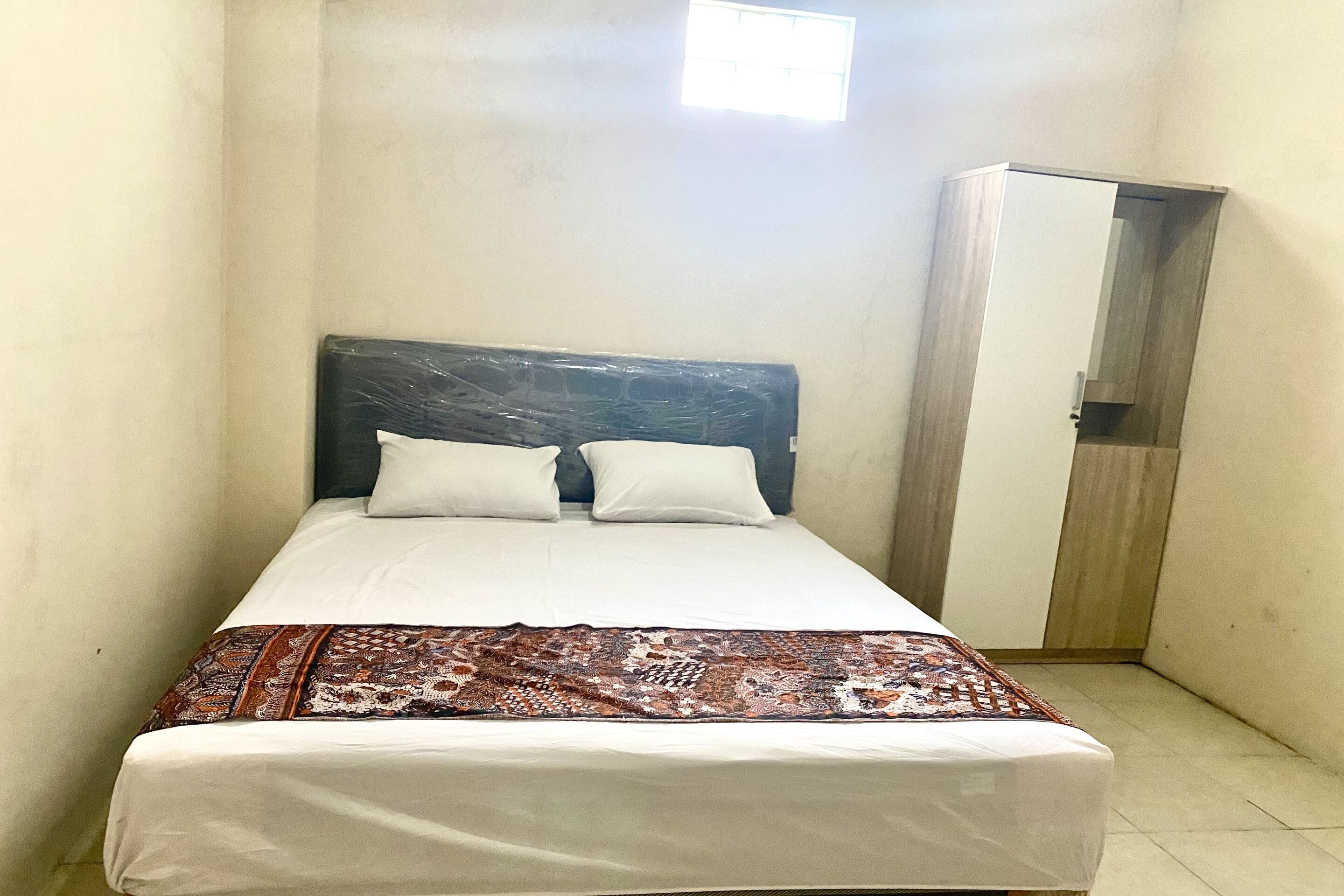 A single bed with a patterned bedspread, a wooden headboard, and a white pillow.