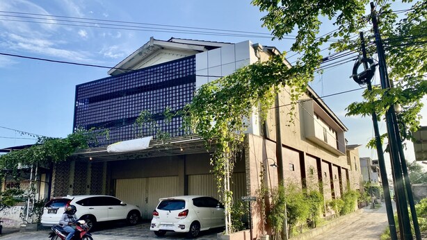 A modern building with a large garage door, parked cars, and a motorcycle on the street. - Hotel O Delia Inn Syariah (Klaten)