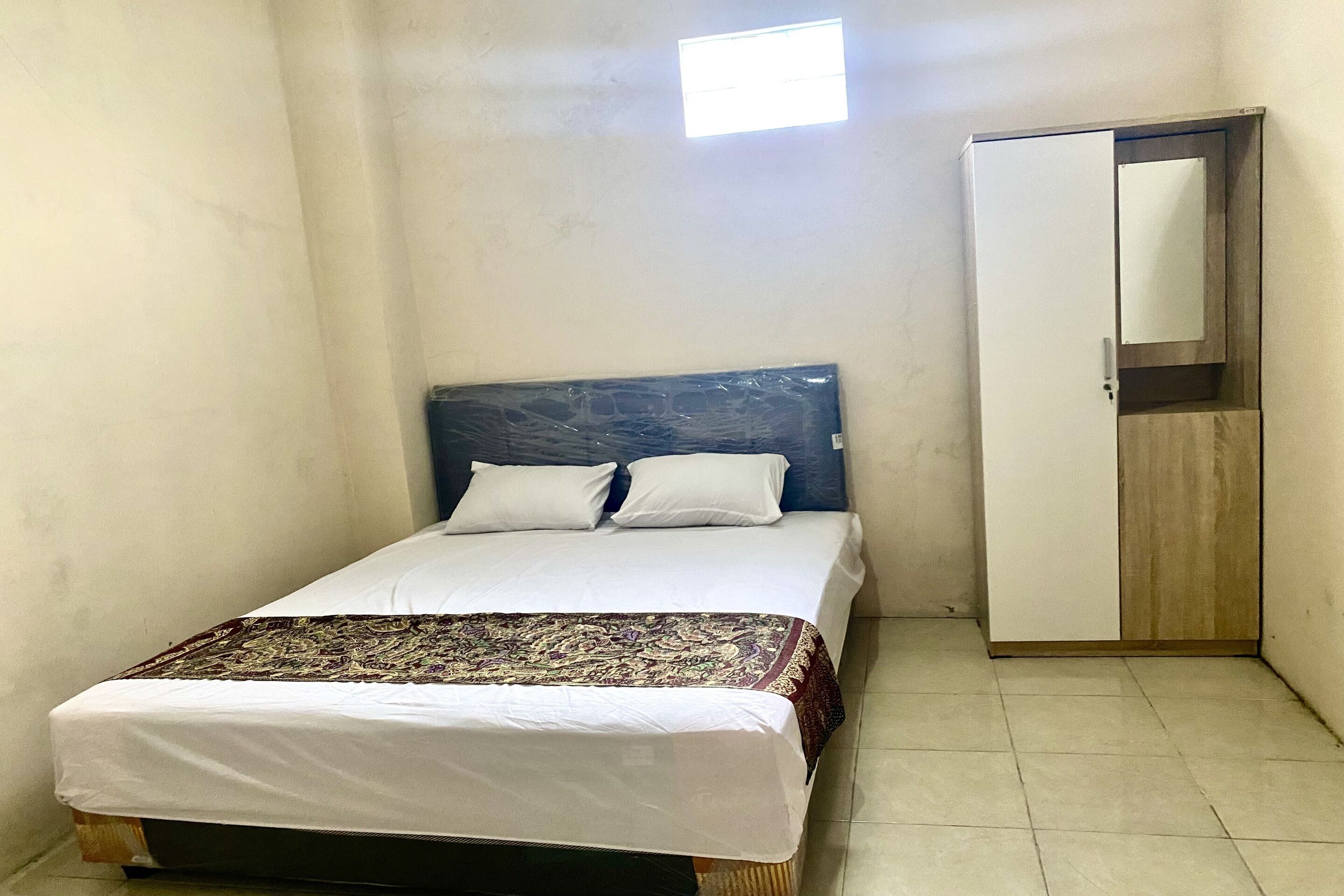 A small, single-bed room with a wooden wardrobe and a small window.