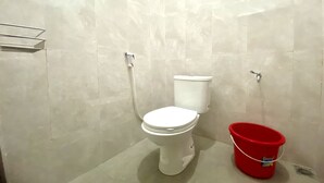 A bathroom with a white toilet, a red bucket, and a metal shelf. - Hotel O Delia Inn Syariah (Klaten)