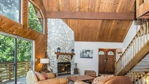 A spacious living room with a stone fireplace, leather sofas, and a wooden staircase. - Lake cabin w/ big pines close to lake and village (Lake Arrowhead)