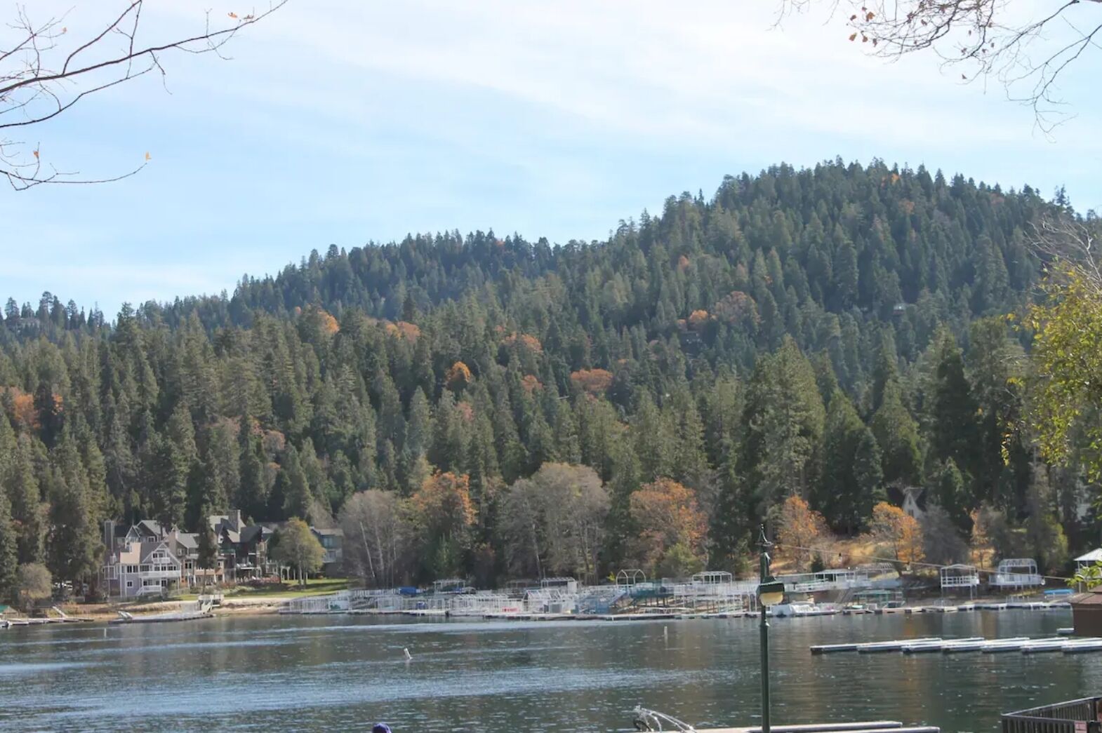 Une vue sur le lac, avec une colline boisée, des bateaux amarrés et un petit bâtiment.
