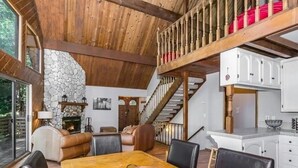 A spacious living area with a stone fireplace, wooden ceiling, and a dining table with chairs. - Lake cabin w/ big pines close to lake and village (Lake Arrowhead)