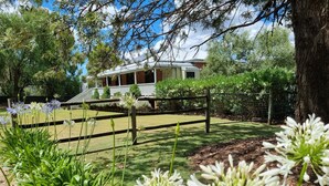 Uma casa com varanda, cercada por um quintal com grama e árvores.