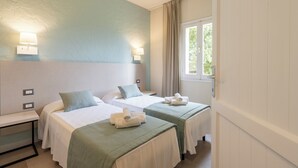 Habitación de hotel con dos camas, cada una con cubrecama verde y ropa de cama blanca. Hay dos lámparas de pared a cada lado de las camas, y una ventana con cortinas a la derecha.