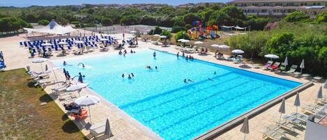 Uma piscina retangular grande, rodeada por espreguiçadeiras e guarda-sóis, com vista para uma área residencial ao fundo.
