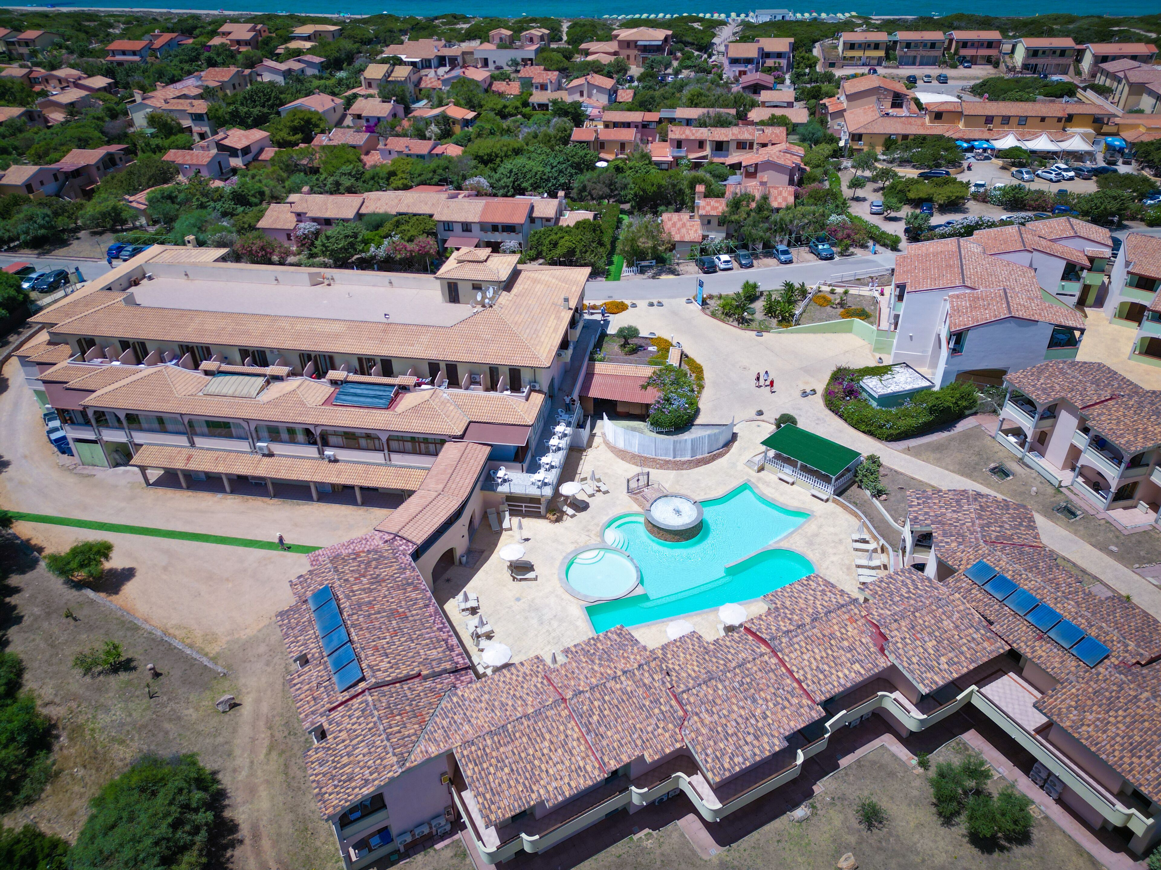 Luchtbeeld van een resort met meerdere gebouwen, een centraal gelegen zwembad en een parkeerplaats.