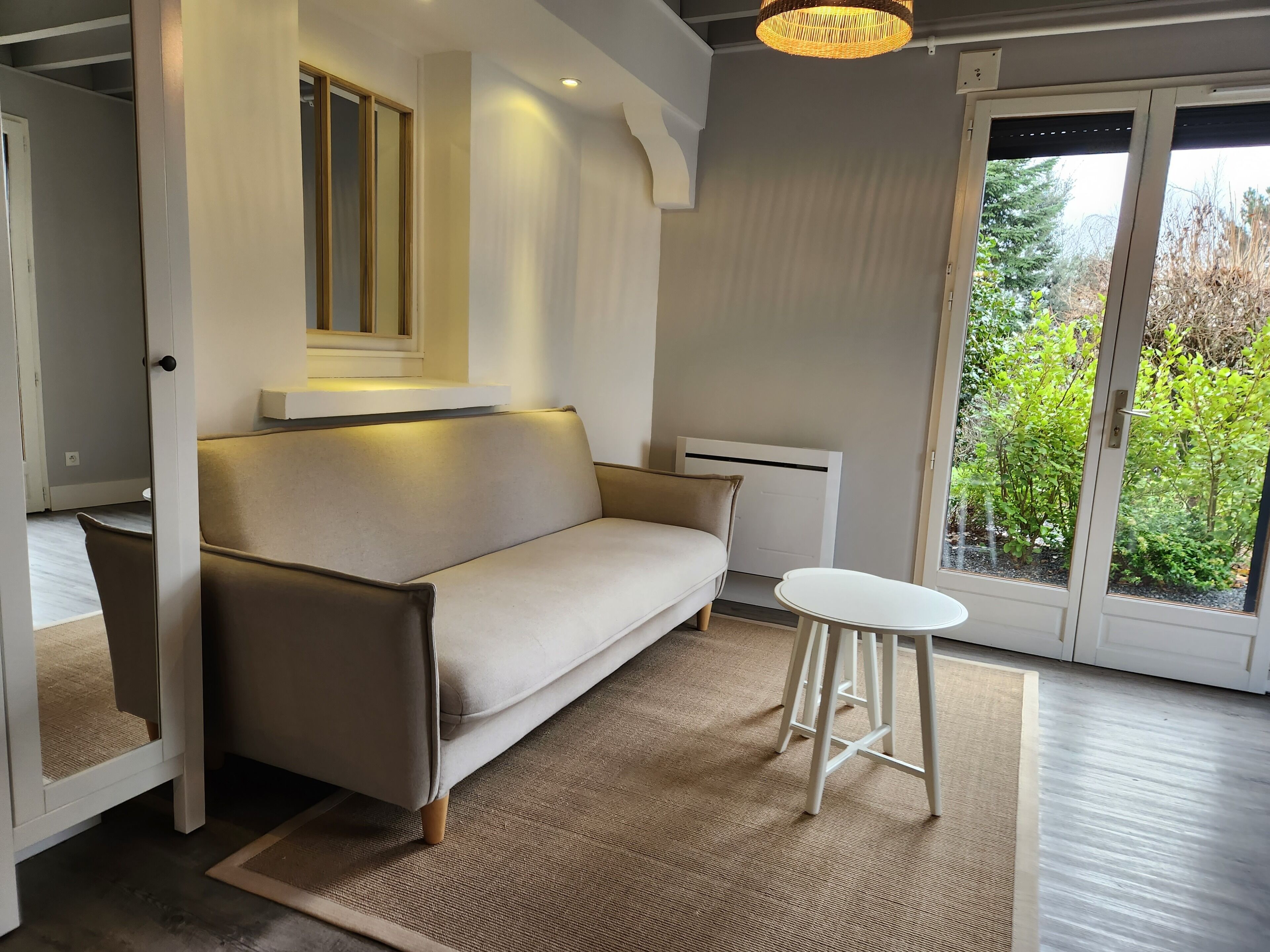 Un salon moderne avec un canapé, une petite table et une vue sur la verdure grâce à une porte vitrée.
