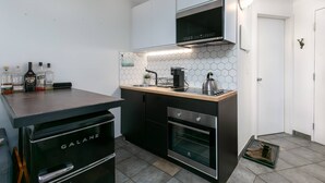 Una cocina moderna con armarios negros, una encimera de madera, horno integrado y microondas. Hay botellas sobre la encimera y una pequeña planta.