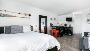 Un dormitorio moderno con una cama grande, una zona de cocina con taburetes rojos y un sofá gris.