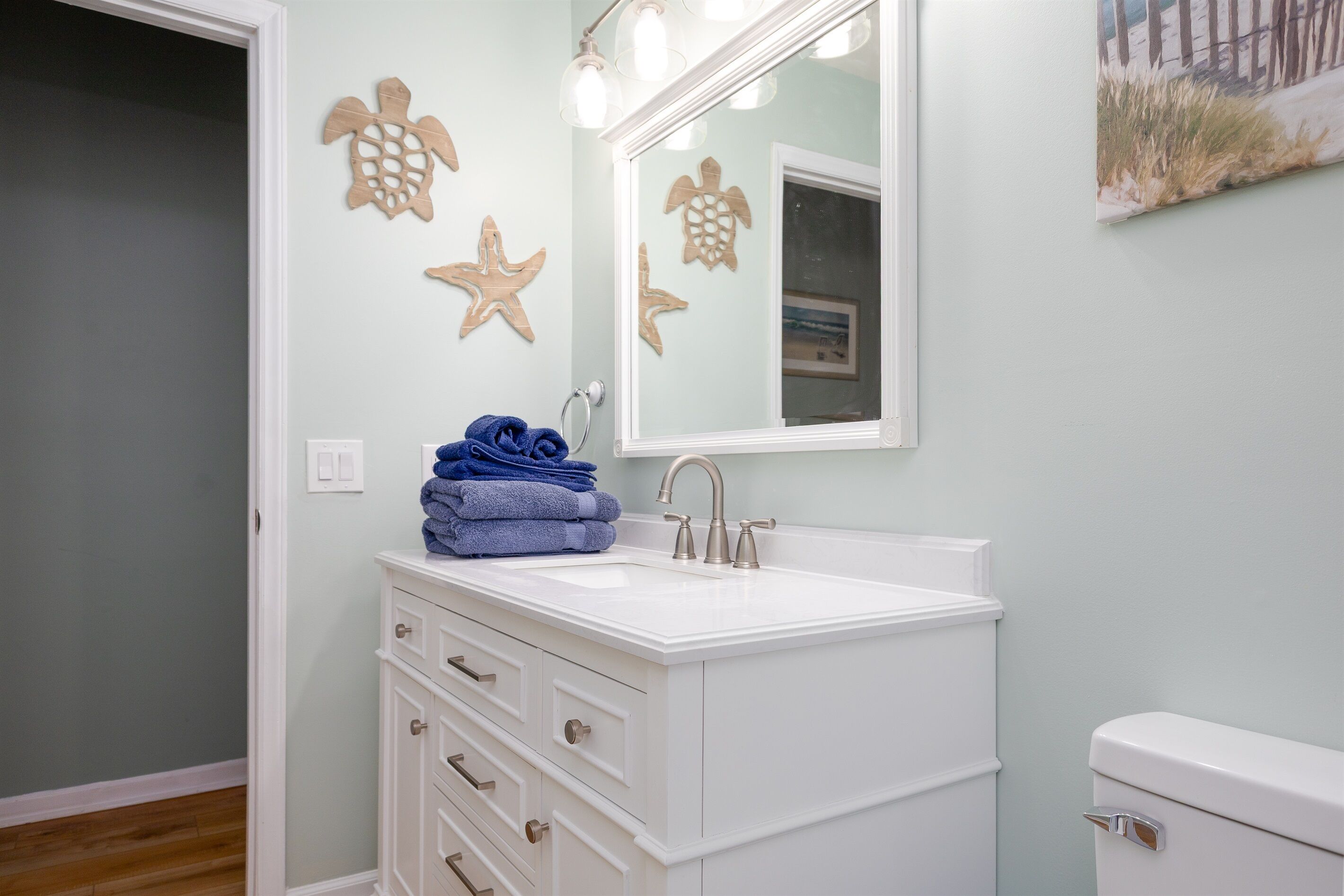 Une salle de bain avec un meuble-lavabo blanc, un évier et des toilettes. Les murs sont décorés de motifs en bois et un tableau encadré est accroché au-dessus du miroir.