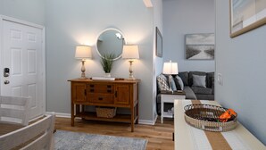 A living room with a wooden cabinet, two lamps, a mirror, a framed picture on the wall, a gray sofa, and a small table with a basket. - "Sun Catcher" -Oceanfront Views | Balcony (North Topsail Beach)