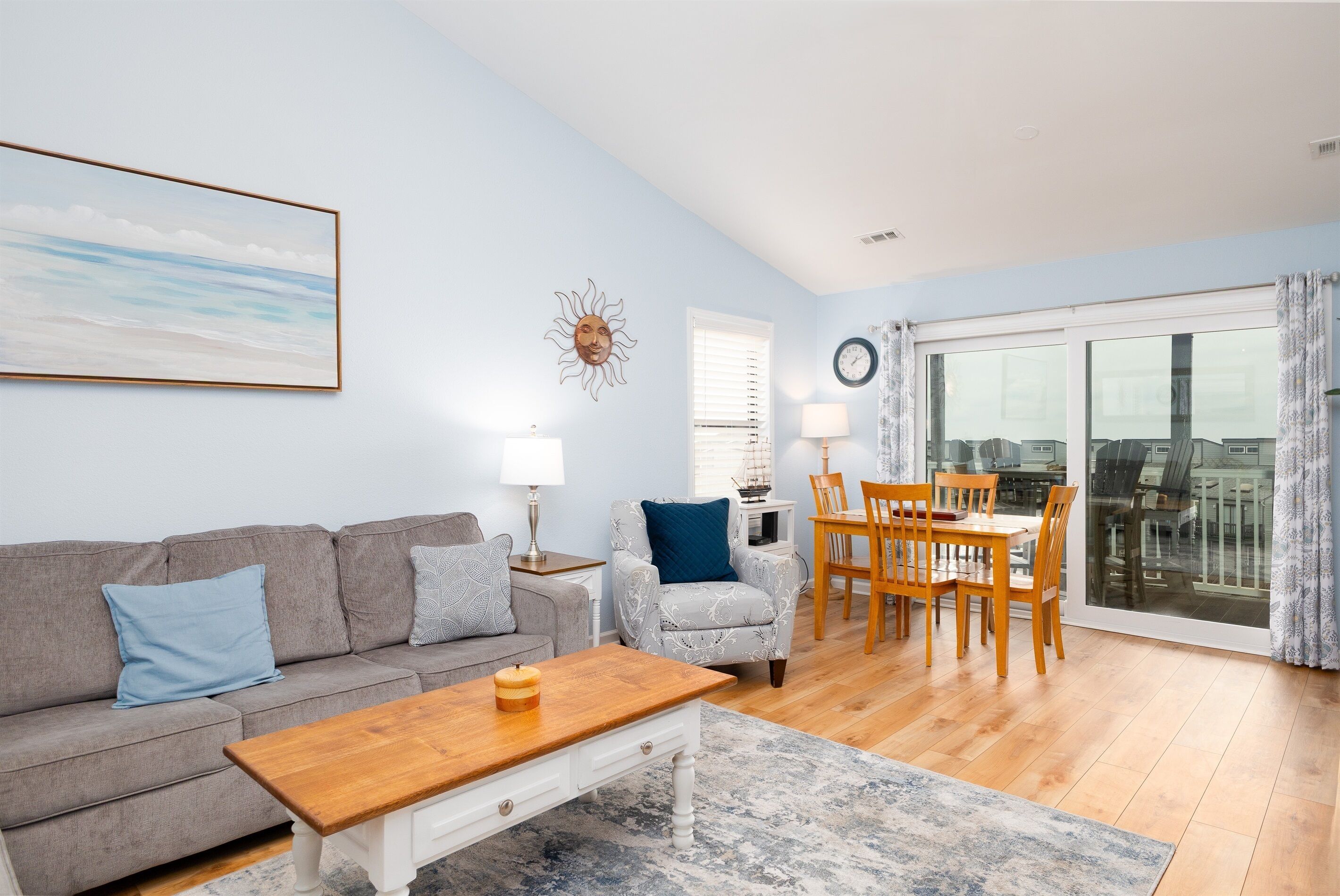 A living room with a sofa, coffee table, dining table, and chairs. There is a window with curtains and a view of the city.