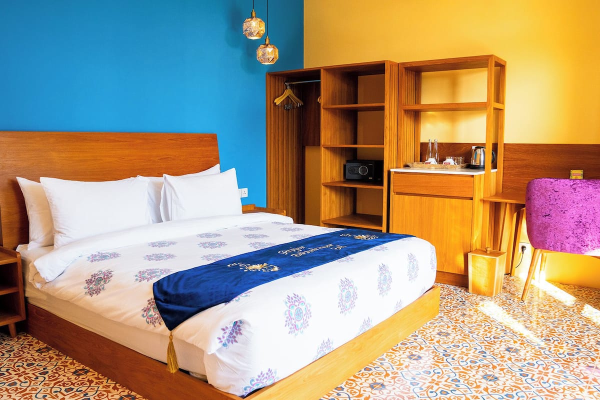 Quarto de hotel com uma cama, guarda-roupa de madeira, rádio e uma pequena mesa com chaleira.